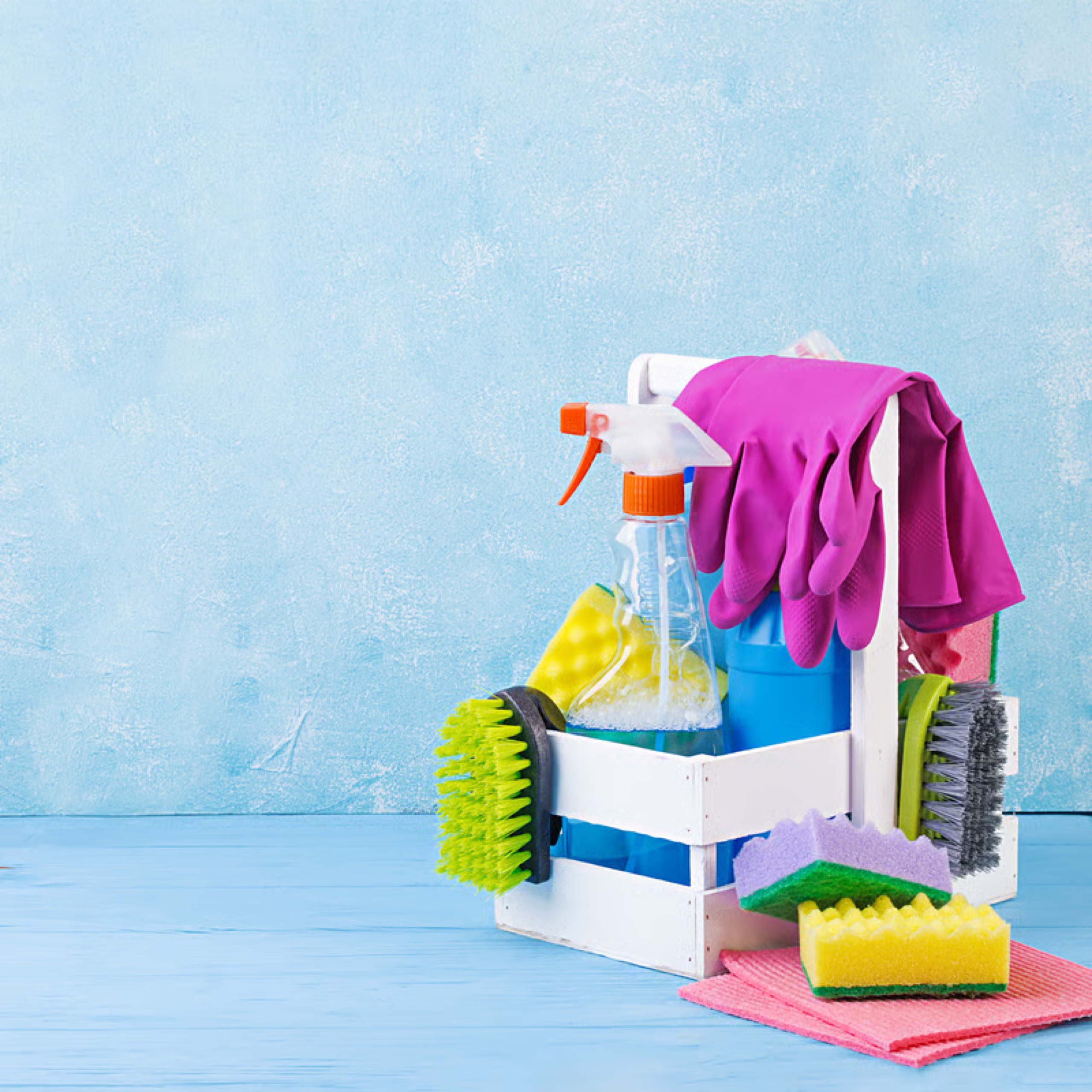 Caddy of cleaning supplies with brushes, sponges, and gloves against a light blue wall