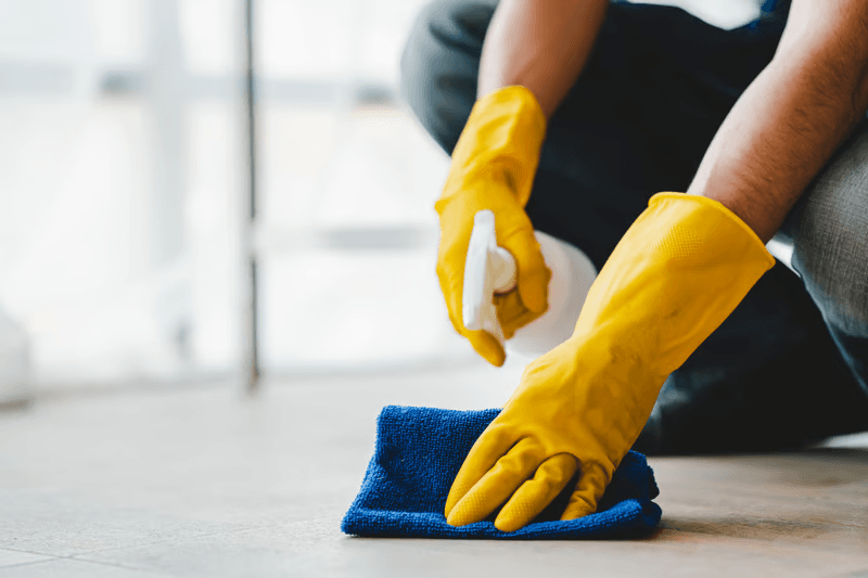 Gloved hands cleaning a floor corner to corner